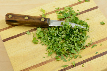 Chopping fresh cilantro on wooden cutting board with kitchen knife