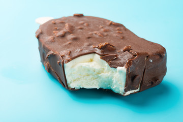 chocolate outer ice cream starts melting with a bite on a blue background
