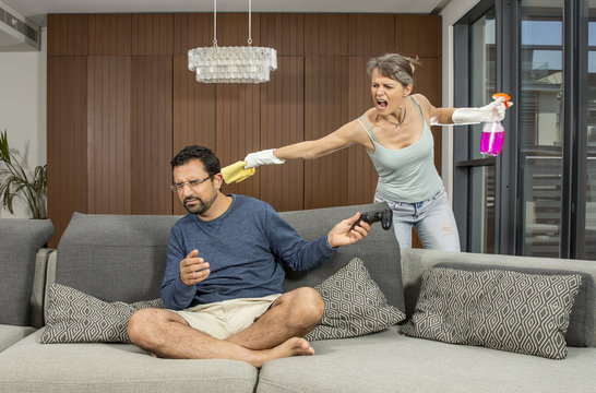 arab man playing a video game while woman is cleaning around him and getting angry