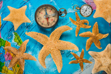 Items for travel: a compass, a pocket watch with a chain on the background of a globe and sea stars.