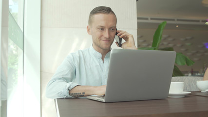 Businessman speaking on smartphone, working with laptop