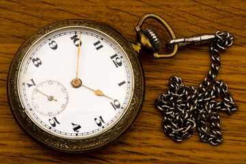 An antique pocket silver watch with a chain on a background of a brown wooden board.