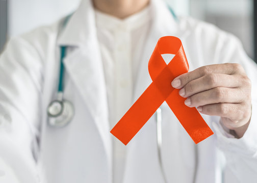 Orange ribbon for raising awareness on Leukemia, Kidney cancer, RDS multiple sclerosis, ADHD illness in doctor's hand (bow isolated with clipping path)