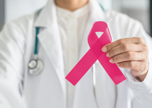 Pink ribbon for breast cancer awareness in doctor's hand, symbolic bow color for raising awareness campaign on women (female)  patient living with breast tumor illness