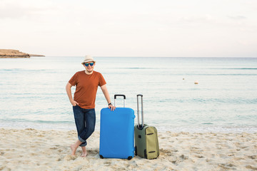 Man in sunglasses and hat with luggage on the sea in summer sunny day