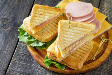 Pressed and toasted double sandwich with ham and cheese, served with lettuce leaves on a kitchen wooden table. Copy space.