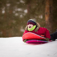 Portrait of cute kid boy sledding down the hill on the board and shouting on a snow winter day. Active child outdoors. Lifestyle concept.