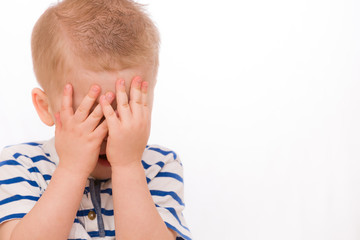 Fototapeta premium Portrait of a small toddler blond boy in a striped shirt hiding himself with hands.. Child crying. Emotions.