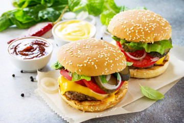 A delicious fresh homemade hamburger on a slate or stone table. Cheeseburger with meat cutlet and vegetables. Street food, fast food.