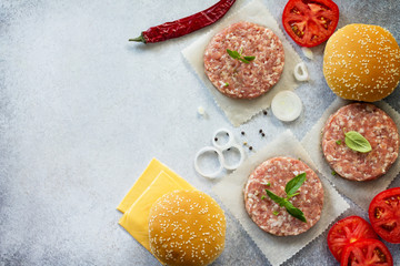 Ingredients for cheeseburger - raw cutlet, bun, cheese, onion, spices, greens and tomatoes. Street food, fast food. Top view with a copy.