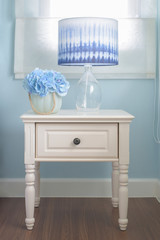 Flower jar and reading lamp on bedside table in light blue interior bedroom