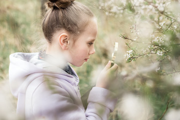 Obraz premium Young blond girl inspecting apple blossoms with a magnifying glass.