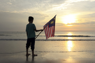 The Concept of Independence Day - a boy holding the Malaysian flag on the shore at sunrise