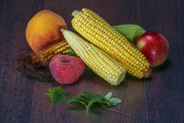 Still life of cobs of corn and fruits on a dark background 