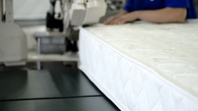 Upholstery is sewed to blank of matrass on the factory closeup. Automatically machine slews ready matrasses.