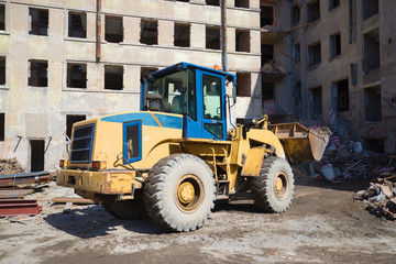 Fototapeta na wymiar Heavy front loader clears debris on the reconstruction of old residential building
