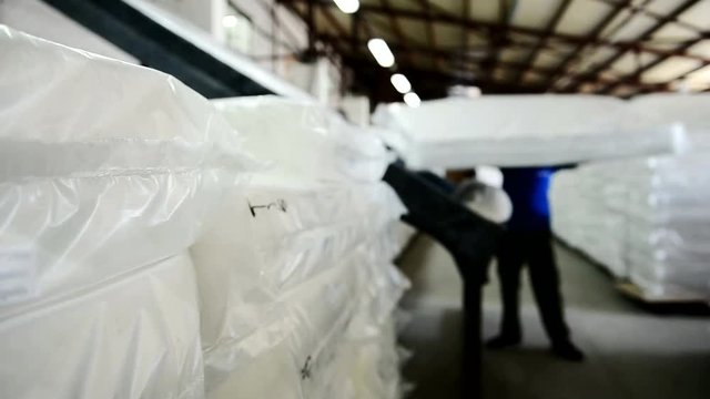 Loader at the plant suffers from complete mattress shop. In a huge workshop stacked white mattresses packed in polyethylene.