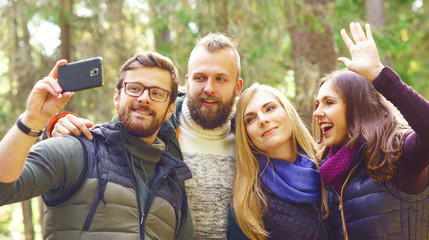 Group of happy friends stopped in forest to take a selfie on a smartphone. Camp, tourism, hiking concept.