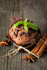 chocolate dark muffin with a leaf of mint on a wooden table with cinnamon, anise, chocolate
