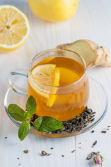 A glass cup of green natural tea with ginger, lemon, mint and honey on wooden rustic background. Healthy drink.