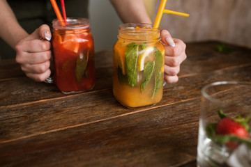 Waiter brings jars of fresh fruit cocktails to customer. Orange and strawberry cold drink with mint and ice on wooden table, refreshment and satisfying thirst in hot weather, free space