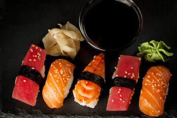Sashimi and sushi rolls on a stone slatter. Sushi set with salmon, prawns, soy souce, wasabi and ginger. Traditional Japanese cuisine.