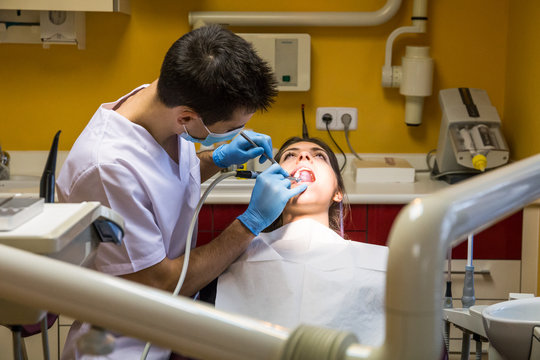 Professional dentist applying drill device to woman while oral cure procedure.