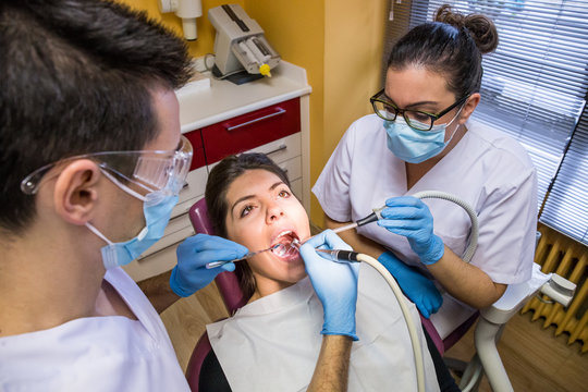 From above dentist and assistant providing oral treatment for female client in cabinet.