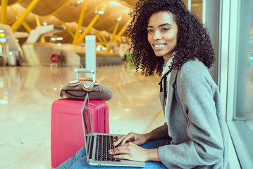 black woman working with laptop at the airport waiting at the window