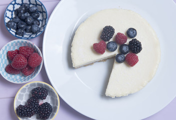 Vanilla cheesecake with a slice missing with blueberries, blackberries and raspberries