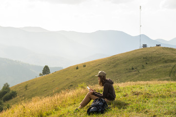 Freelancer girl works with tablet online outdoors. Hiker female uses portable tablet pc in mountains near cellphone tower