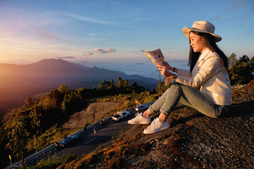 A woman siting on top of the hill reading a map and enjoying the view of the sunrise in winter