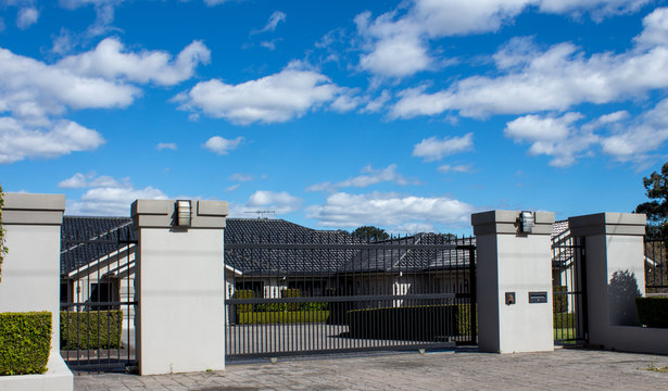 Black Metal Driveway Entrance Gates Set In Brick Fence With Private House In Background