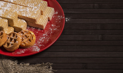 A plate of Belgian wafers and cubic wafers for tea on a red plate sprinkled with powdered sugar