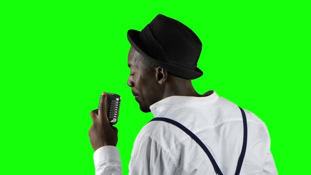 Man african american the view from the back standing at the microphone professionally singing in a recording studio. Green screen. Close up