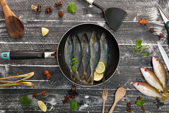 Fresh fish in black frying pan on dark black background, Fish with spices and vegetables, cooking background concept.