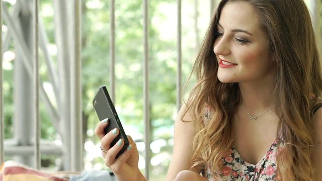 Pretty brunette in floral clothing looks happy while doing selfies on smartphone, steadycam shot
