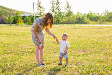 Fototapeta premium Happy young mother playing with her little baby son on sunshine warm autumn or summer day. Beautiful sunset light in a countryside field. Happy family concept