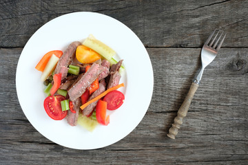 Teller mit Salat vom Rindfleisch in Streifen und Tomaten, Paprika und Gurken