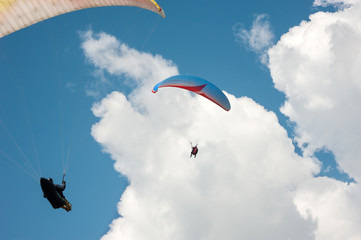 Two paragliders flying in the blue sky against the background of clouds.