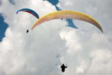 Two paragliders flying in the blue sky against the background of clouds.