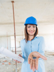 Woman engineer smiling and holding key of the new home in the hand.Construction site in the background.Shallow doff