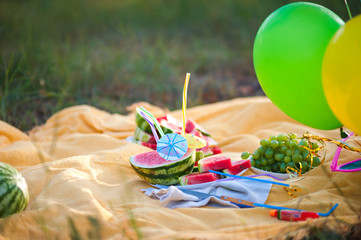 Naklejka premium Many cut pieces of watermelon with colorful tubes and umbrellas. Cocktail of watermelons on a yellow plaid. Picnic in the summer with watermelons, balloons, grapes.