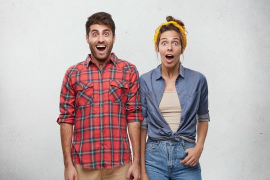 Surprise and astonishment concept. Picture of funny emotional young European couple wearing fashionable clothing expressing shock and full disbelief, amazed with astonishing unexpected news