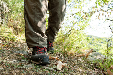 Hiking shoes with red laces and legs wearing long brown trousers of an hiker walking on a path in the wood - 169277978
