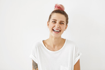 Smiling positive female with attractive look, wearing loose white T-shirt, posing against white...
