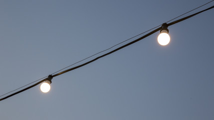 Dettaglio di lampadine accese e appese ad un filo in maniera artigianale durante le prime ore della...