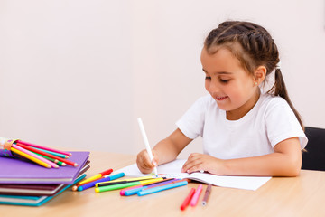 happy cute little girl doing school homework studying in living room at home and writing english class notebook learning knowledge.