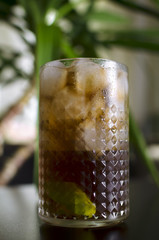 Cocktail cube libre on black table with palm tree on background