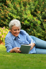 Glückliche Seniorin liest ein Buch im Garten in ihrer Freizeit im Sommer